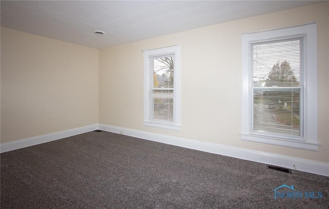 unfurnished room with visible vents, baseboards, and dark carpet