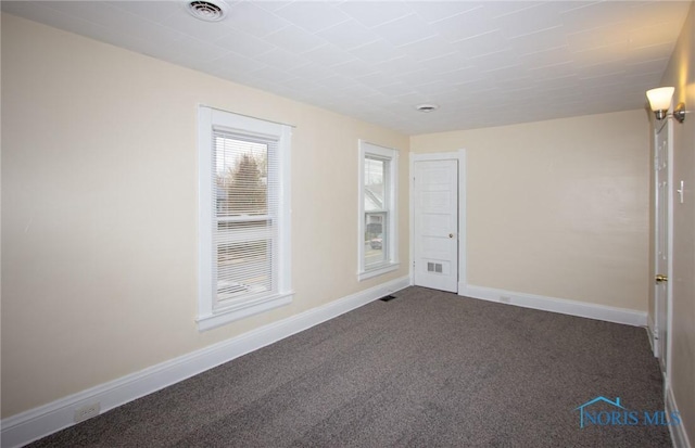 spare room with baseboards, visible vents, and dark colored carpet