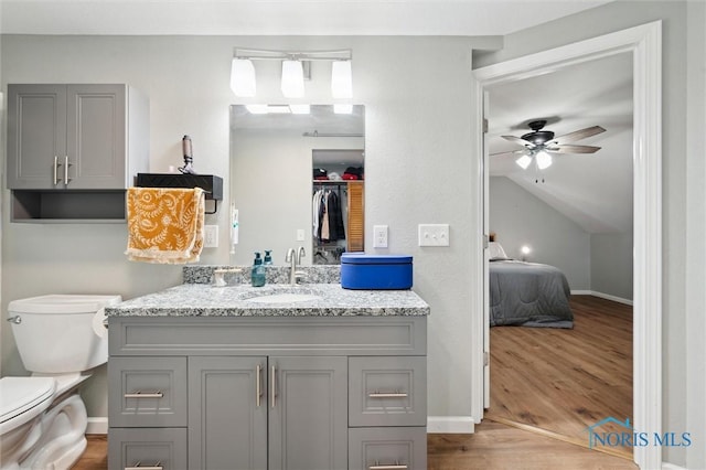 bathroom with ceiling fan, toilet, lofted ceiling, wood finished floors, and vanity