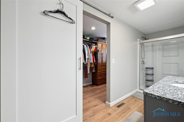 full bath featuring visible vents, a walk in closet, wood finished floors, a shower stall, and baseboards