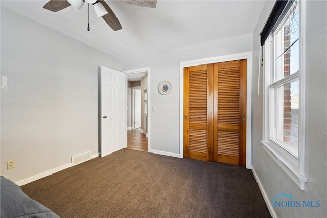 unfurnished bedroom with visible vents, baseboards, a closet, a ceiling fan, and dark colored carpet