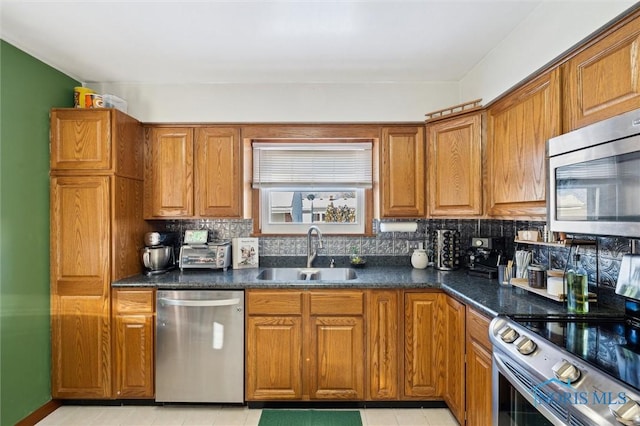 kitchen with dark countertops, decorative backsplash, brown cabinets, stainless steel appliances, and a sink