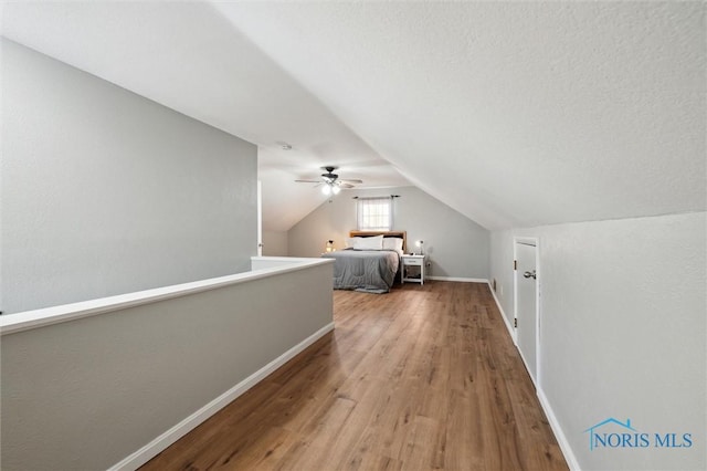 interior space featuring baseboards, a textured ceiling, wood finished floors, and vaulted ceiling