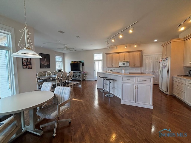 kitchen featuring a kitchen bar, light brown cabinetry, backsplash, dark wood-style floors, and white fridge with ice dispenser