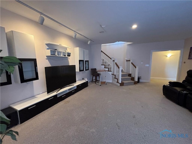 living room with light carpet, track lighting, stairs, and baseboards