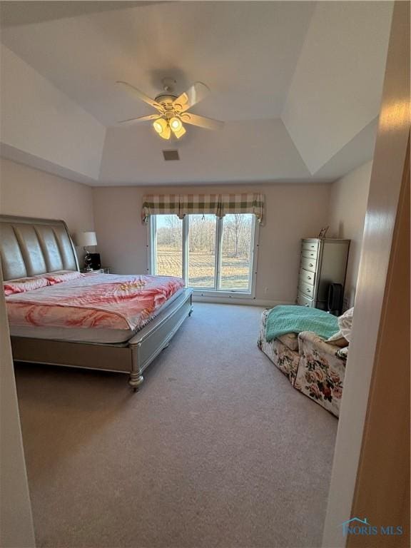 carpeted bedroom with visible vents, a raised ceiling, and ceiling fan