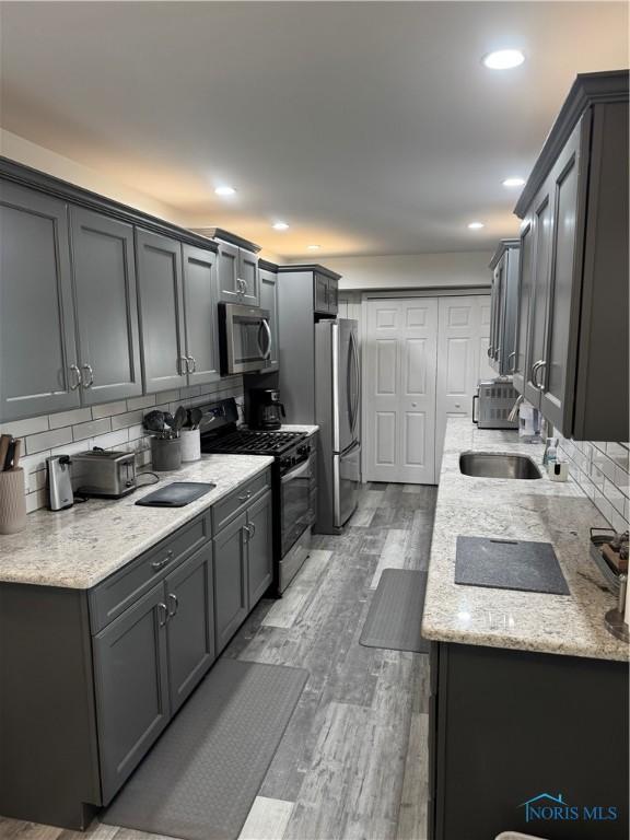 kitchen with light stone counters, recessed lighting, decorative backsplash, appliances with stainless steel finishes, and light wood-type flooring