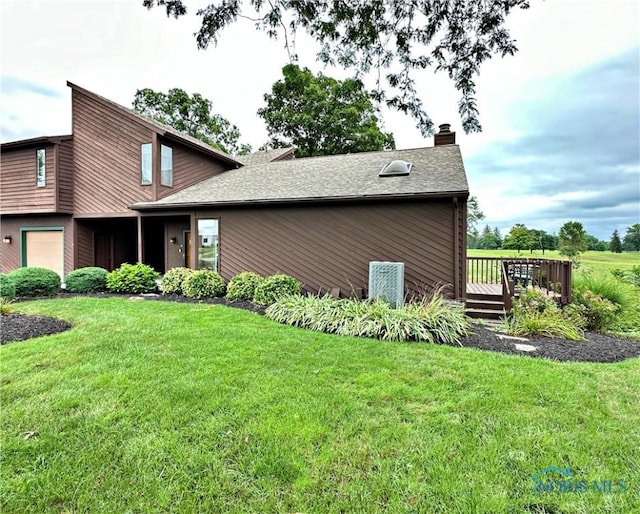 view of front facade with a deck, a front lawn, roof with shingles, a garage, and a chimney