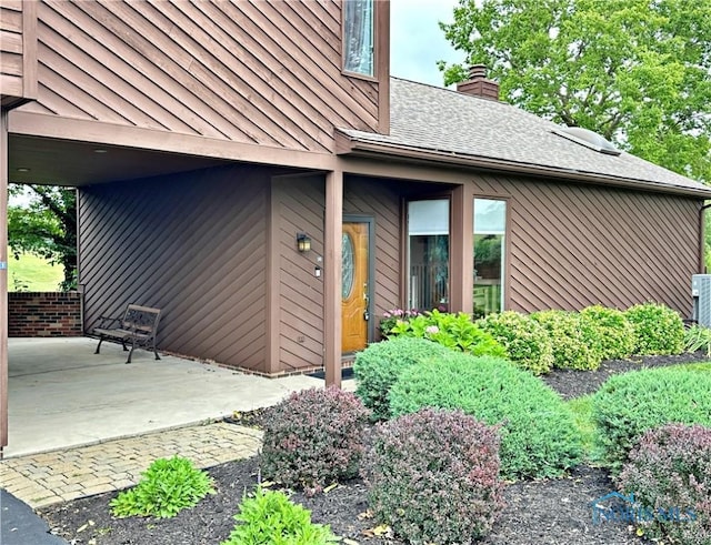 doorway to property featuring a patio, roof with shingles, a standing seam roof, a chimney, and metal roof