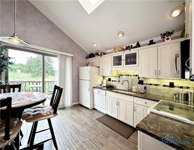 kitchen with a sink, white appliances, vaulted ceiling with skylight, and white cabinetry