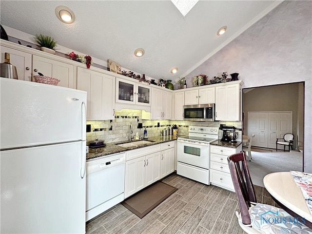 kitchen with white appliances, lofted ceiling, a sink, decorative backsplash, and white cabinets