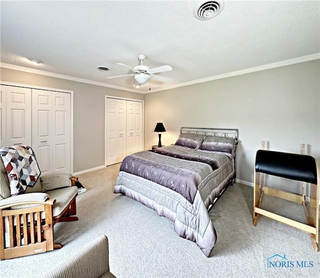 carpeted bedroom featuring visible vents, multiple closets, a textured ceiling, and crown molding