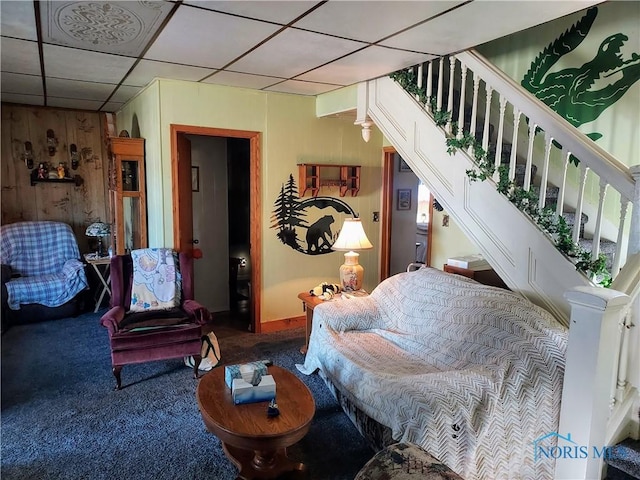 living room with wooden walls, a paneled ceiling, stairs, and carpet