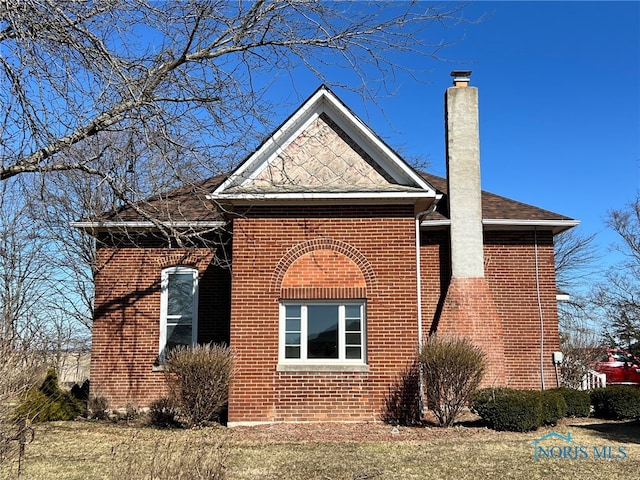 view of home's exterior featuring a shingled roof, brick siding, and a chimney