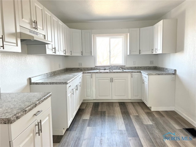 kitchen with visible vents, dark wood-type flooring, under cabinet range hood, a sink, and white cabinets