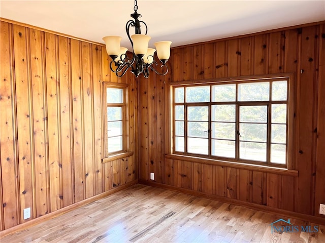 empty room featuring baseboards, an inviting chandelier, wood walls, and light wood finished floors