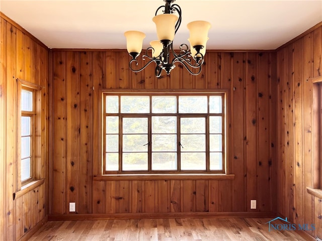 empty room with an inviting chandelier, wooden walls, light wood-style floors, and baseboards