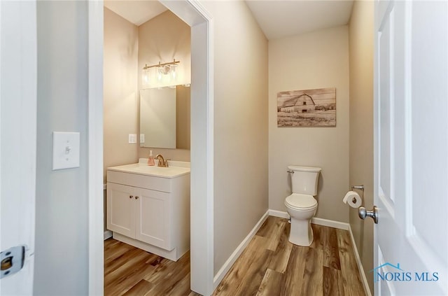 half bath with toilet, vanity, baseboards, and wood finished floors