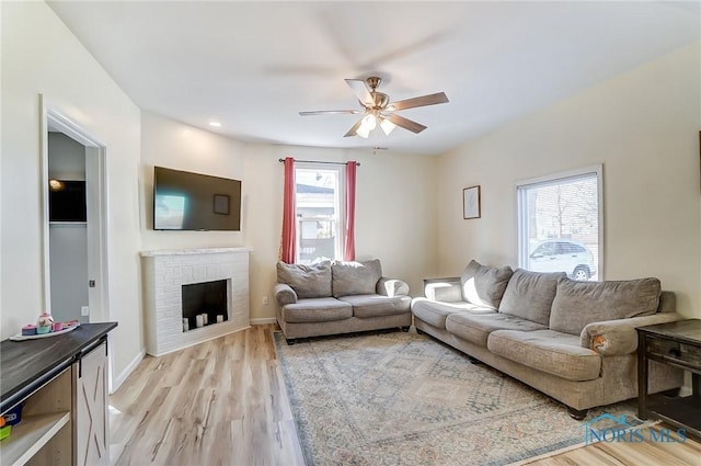 living area with a ceiling fan, baseboards, light wood-style floors, and a fireplace