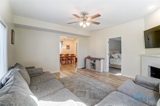 living area featuring ceiling fan, a brick fireplace, baseboards, and wood finished floors