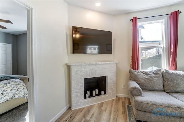 living area with a fireplace, wood finished floors, baseboards, and a ceiling fan