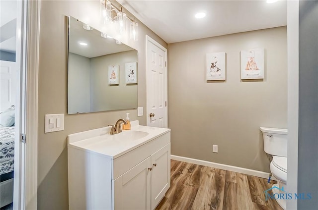 bathroom with vanity, toilet, wood finished floors, and baseboards