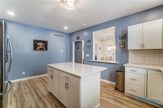 kitchen featuring visible vents, tasteful backsplash, stainless steel fridge, light wood finished floors, and light countertops