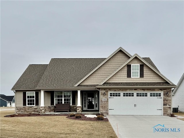 craftsman house with a front lawn, roof with shingles, a garage, stone siding, and driveway