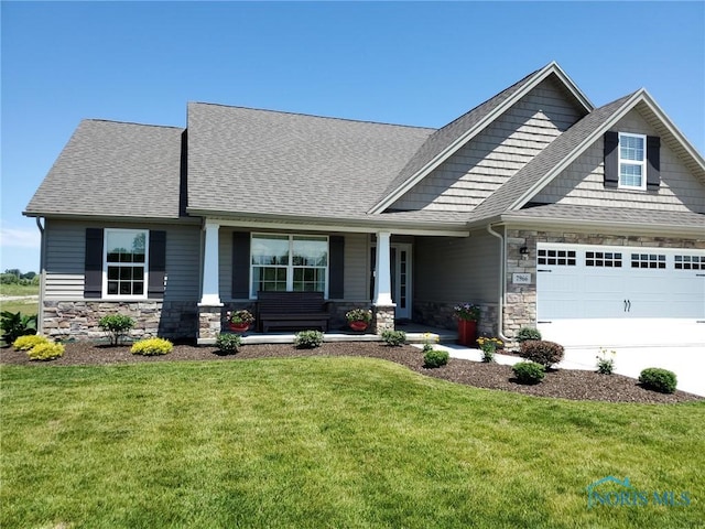 craftsman-style house featuring a front yard, covered porch, driveway, stone siding, and an attached garage