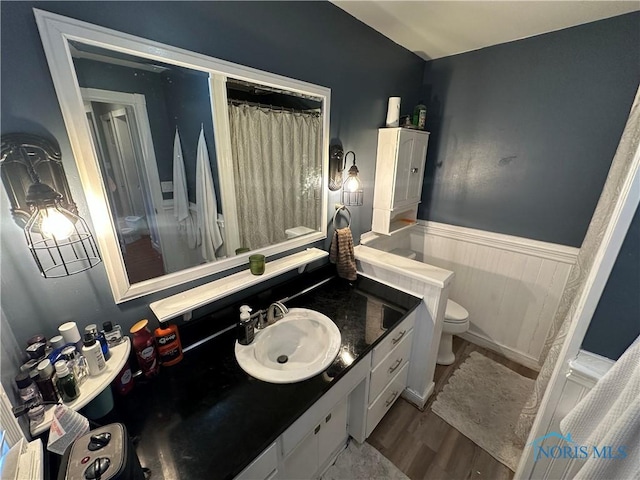 full bath featuring a wainscoted wall, toilet, wood finished floors, and vanity