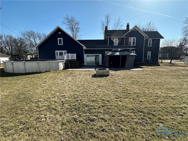 rear view of property with an outdoor pool, a gazebo, and a chimney