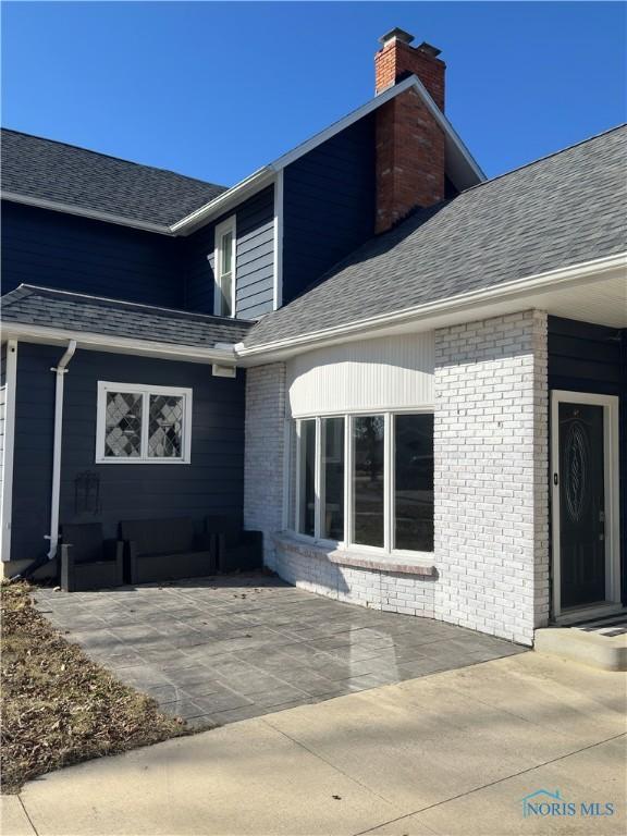 doorway to property with brick siding, a chimney, and a shingled roof