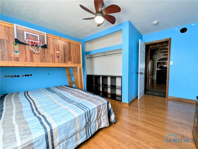 bedroom featuring a ceiling fan, baseboards, wood finished floors, a closet, and a textured ceiling