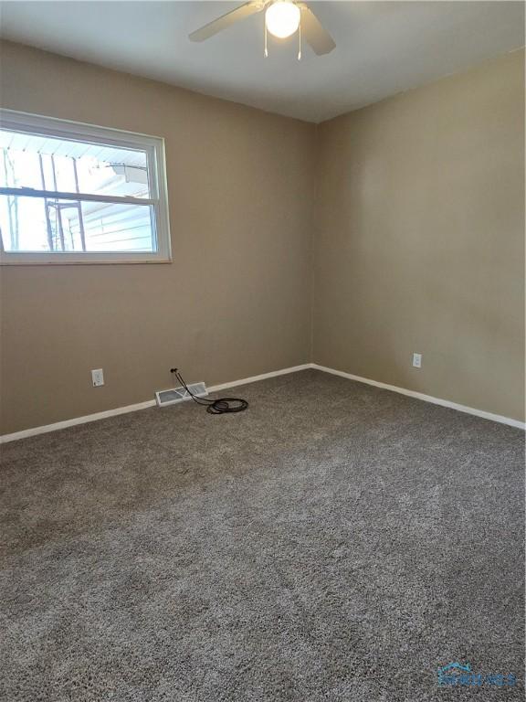 carpeted spare room featuring visible vents, baseboards, and a ceiling fan