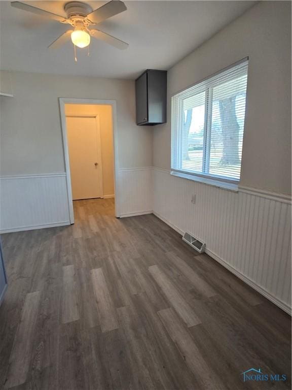 interior space featuring a wainscoted wall, wood finished floors, visible vents, and a ceiling fan