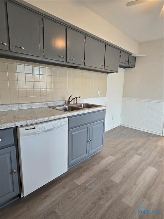 kitchen with gray cabinetry, a sink, dark wood finished floors, white dishwasher, and light countertops