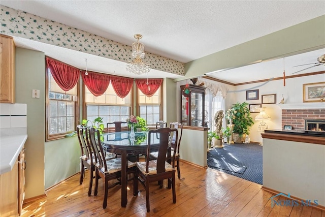 dining room featuring baseboards, wood-type flooring, a textured ceiling, and a brick fireplace