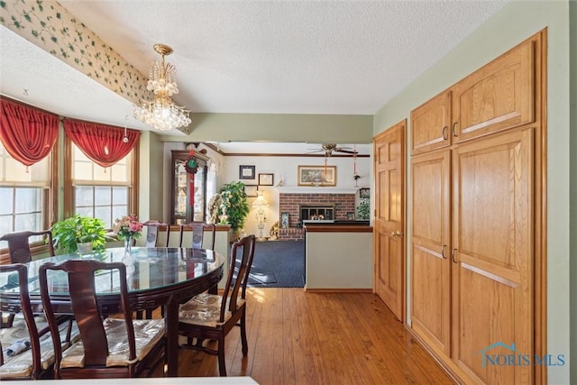 dining area with ceiling fan with notable chandelier, a fireplace, light wood-type flooring, and a textured ceiling