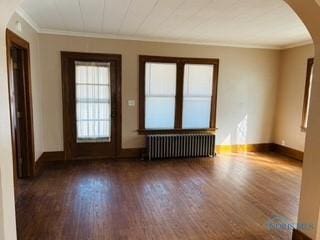 empty room featuring radiator, wood finished floors, baseboards, arched walkways, and ornamental molding