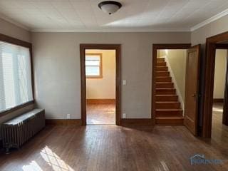 spare room featuring crown molding, baseboards, stairway, radiator heating unit, and wood finished floors