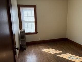 spare room with radiator heating unit, baseboards, and wood finished floors