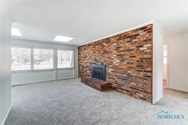 unfurnished living room featuring baseboards, a wood stove, a skylight, a textured ceiling, and carpet flooring