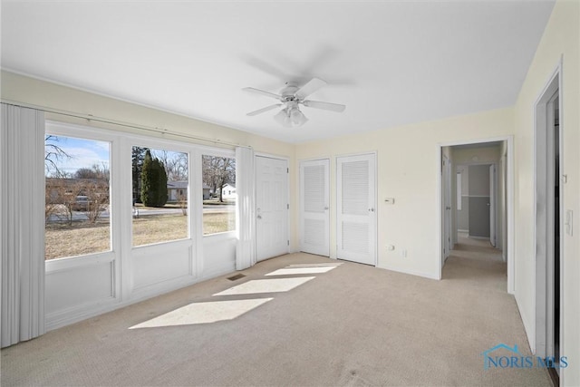 unfurnished bedroom with light carpet, visible vents, two closets, and ceiling fan