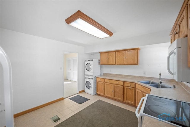 kitchen featuring baseboards, light tile patterned floors, white appliances, stacked washer / drying machine, and a sink