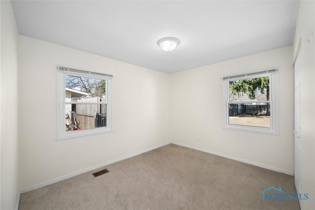 carpeted spare room with visible vents, a healthy amount of sunlight, and baseboards