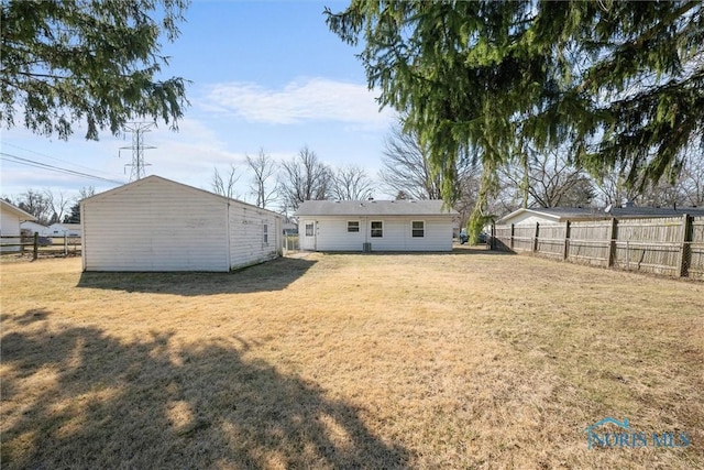 rear view of property with a lawn, an outdoor structure, and fence