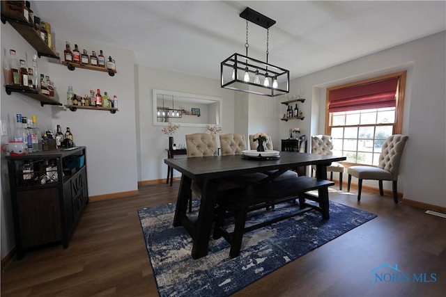 dining room with visible vents, baseboards, wood finished floors, and a dry bar