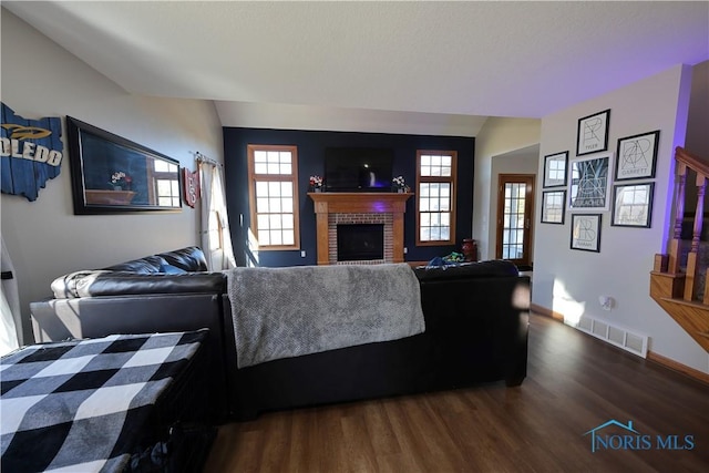 living area featuring visible vents, dark wood-style floors, a fireplace, baseboards, and vaulted ceiling