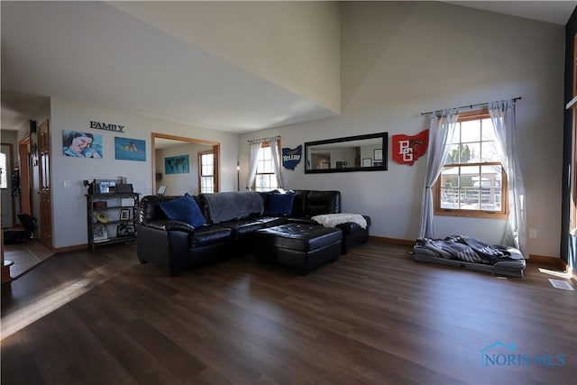 living room with dark wood-type flooring, baseboards, and a towering ceiling