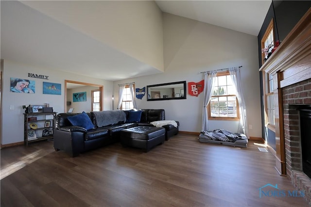 living area with dark wood finished floors, a brick fireplace, baseboards, and high vaulted ceiling